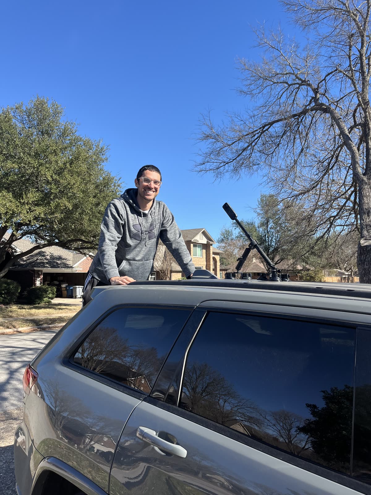 A camera on a mast clamped to the roof rack of an SUV on a residential street, with one of us standing beside it.